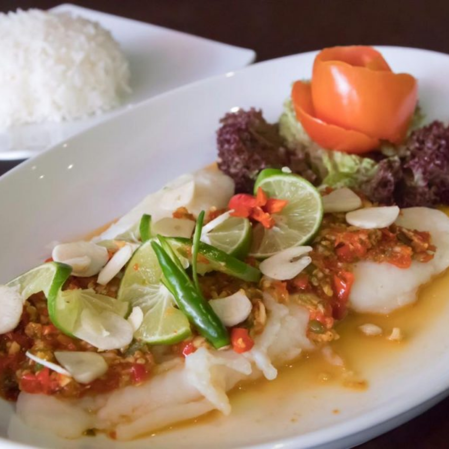 Plated dish with hoki fish, lime wedges, and garnishes on a white plate. - New Zealand Hoki Boneless and Skinless Fillets (4 Pieces/Pack, 400g)