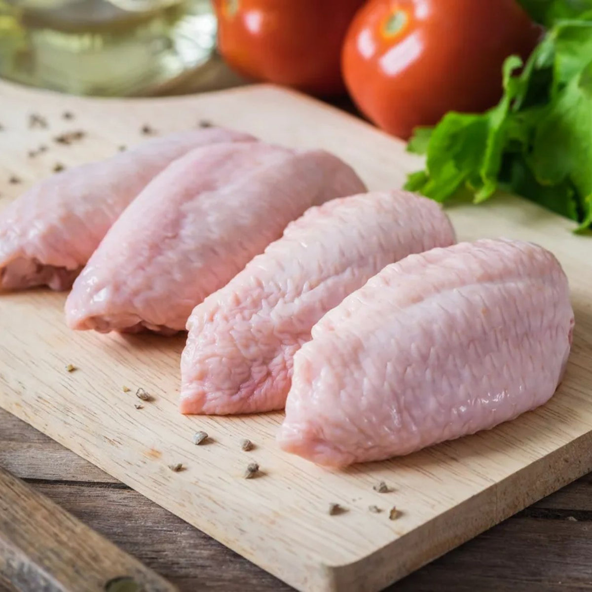 Raw chicken wings on a wooden cutting board with tomatoes and lettuce in the background - Australian Hormone Free Chicken Mid Wings (400g)