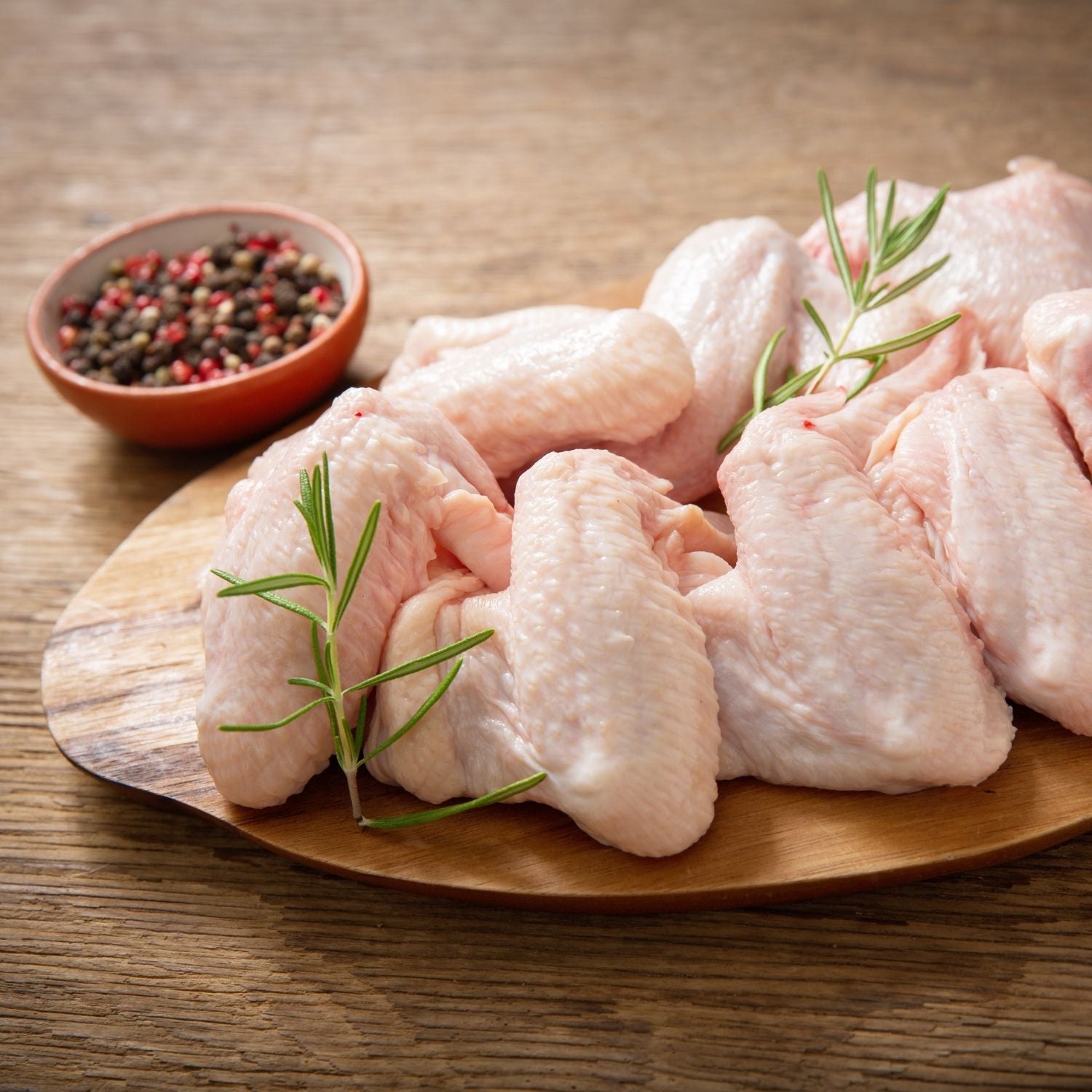Raw chicken wings on a wooden plate with rosemary and a bowl of spices on a wooden surface. - Australian Hormone Free Chicken Whole Wings (400g)