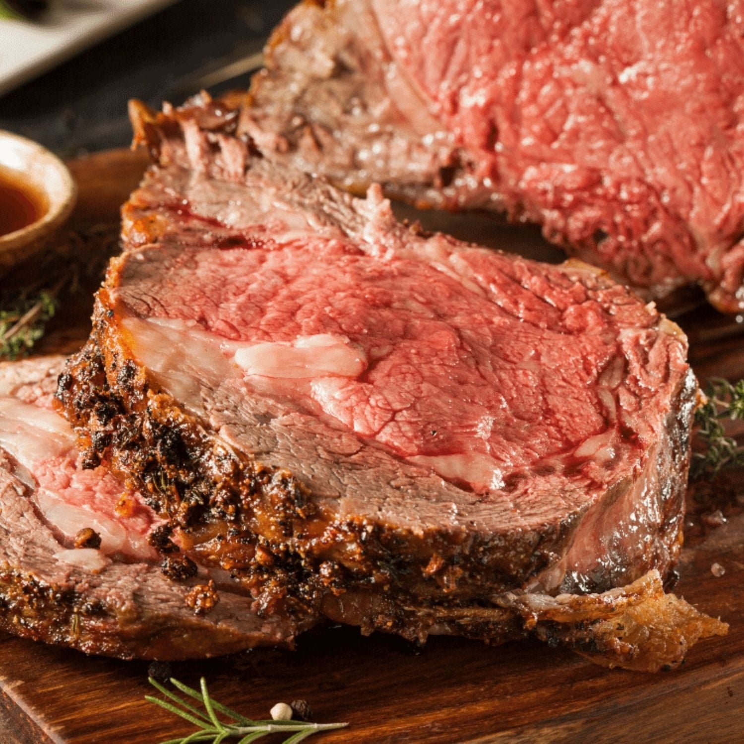 Sliced beef ribeye roast ribeyon a wooden cutting board with a small bowl of sauce in the background. - 澳洲優質黑安格斯肉眼(肋眼,MS 2+,2公斤)