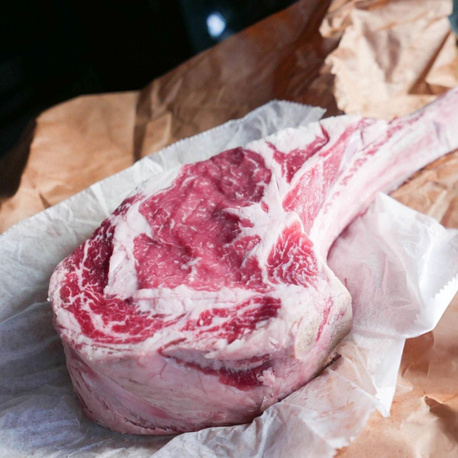 Raw tomahawk steak on a piece of paper with a blurred background - 澳洲優質黑安格斯斧頭扒
