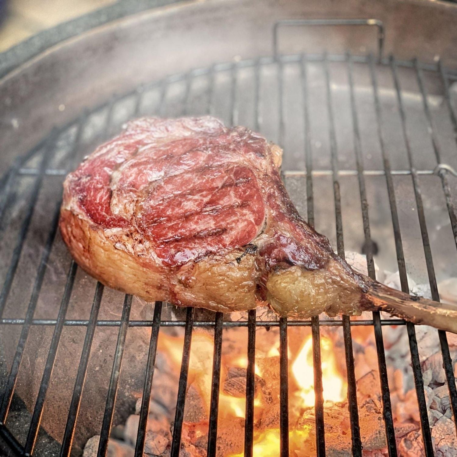Tomahawk steak being grilled over an open flame on a barbecue. - 澳洲優質黑安格斯斧頭扒