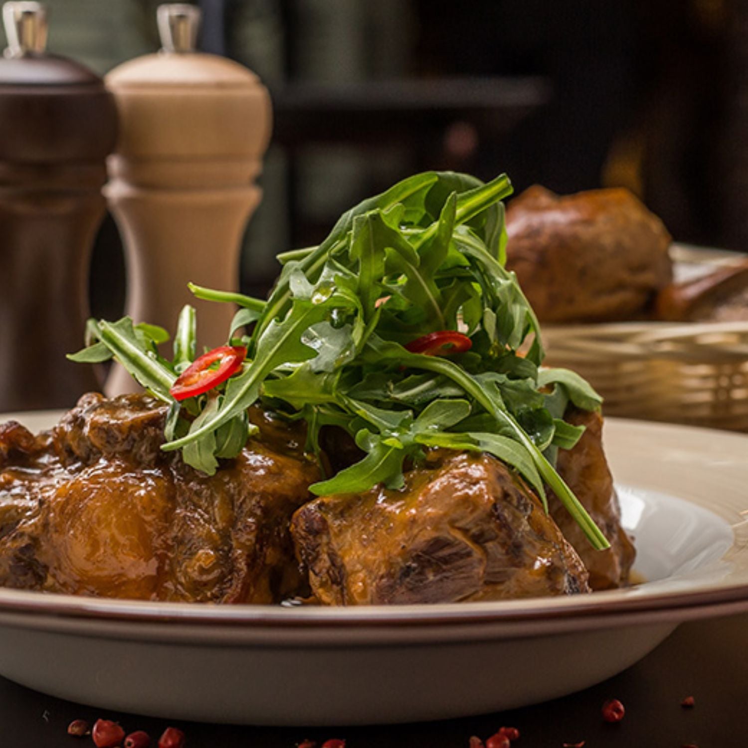 Plated dish of oxtail with greens and red peppers on a table setting. - 澳洲優質牛尾切件 (800克)