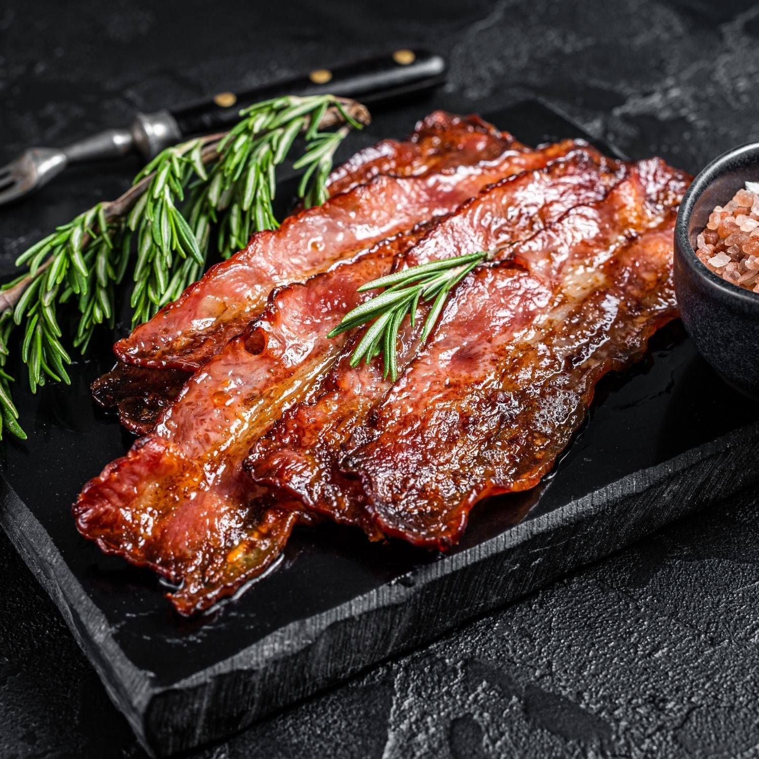 Bacon slices on a black slate board with rosemary and salt. - 荷蘭煙燻五花腩煙肉(200克)