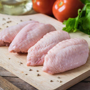 Raw chicken wings on a wooden cutting board with tomatoes and lettuce in the background. - EU Hormone Free Chicken Mid-Wings (908g)