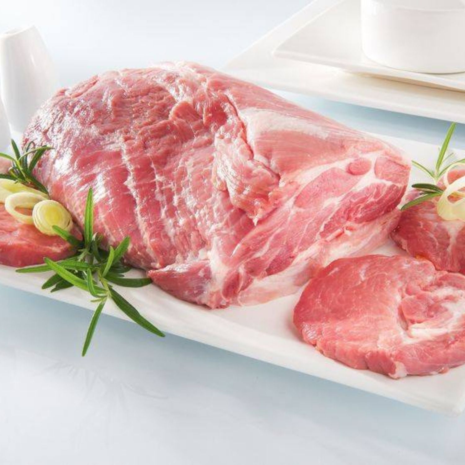 Raw pork collar on a white plate with rosemary and garlic on a light blue background - 歐盟無激素梅花肉(肩膀)(2公斤)|九五折