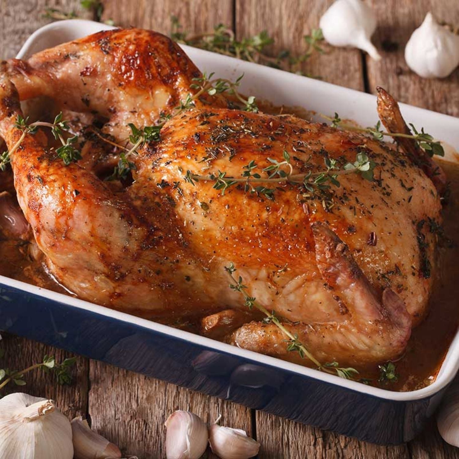 Roasted chicken with herbs in a baking dish on a wooden surface with garlic cloves. - EU Hormone Free Whole Chicken (1.7kg)