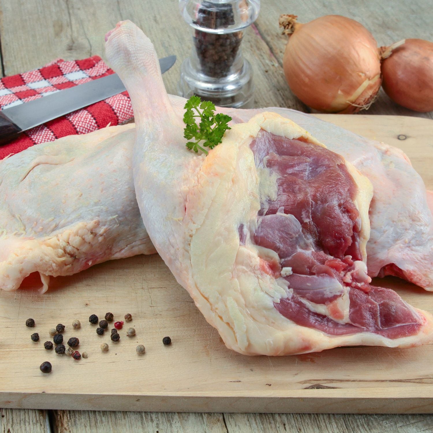 Raw duck legs on a wooden cutting board with spices and onions in the background. - 無激素法國連皮鴨髀