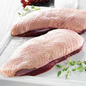 Two raw duck breasts on a white surface with green herbs. - French Hormone Free Moulard Duck Breast Skin-On Boneless Fillet