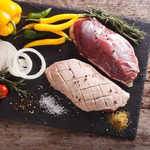 Raw duck breast with vegetables on a dark slate board - French Hormone Free Moulard Duck Breast Skin-On Boneless Fillet