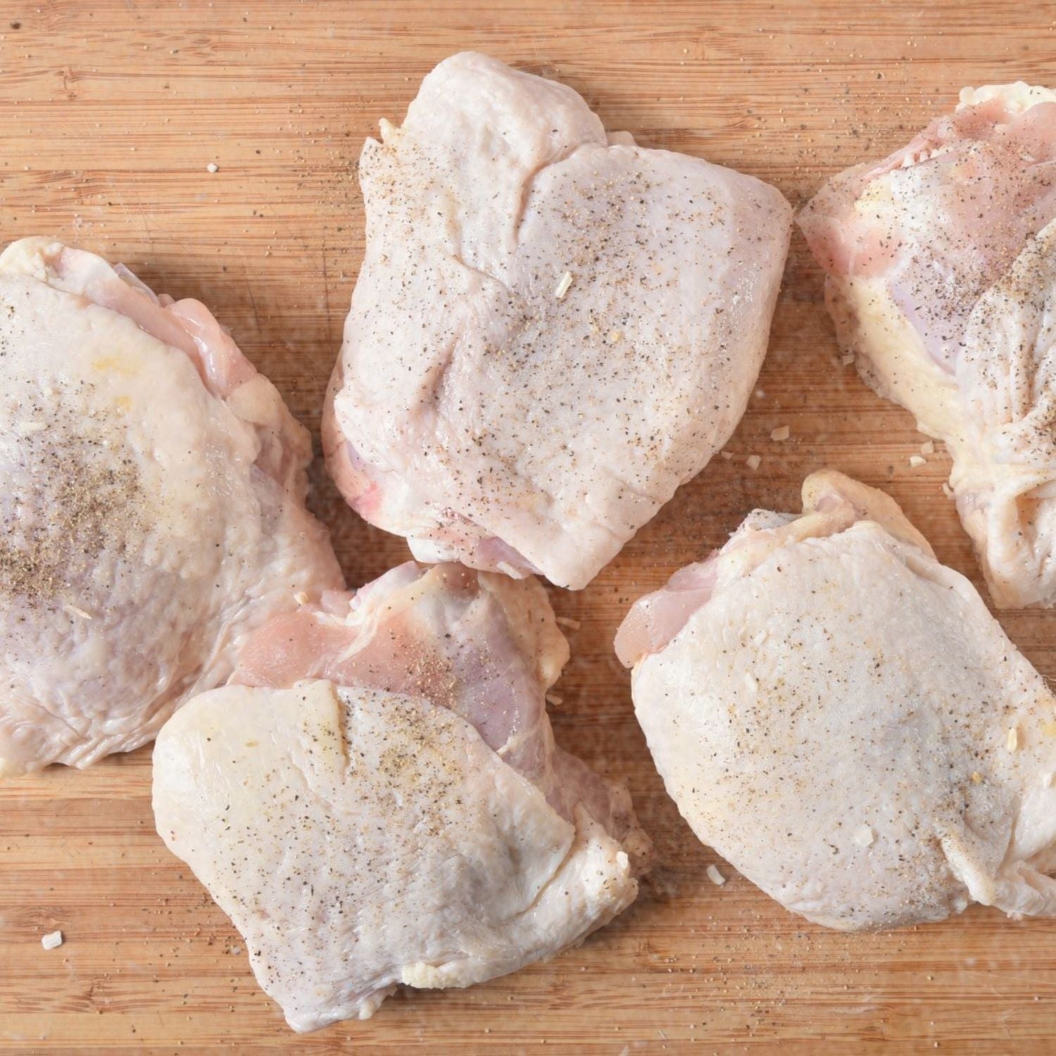Raw chicken thighs on a wooden cutting board with black pepper seasoning - 澳洲無激素連皮雞扒(400克)|買二十送六