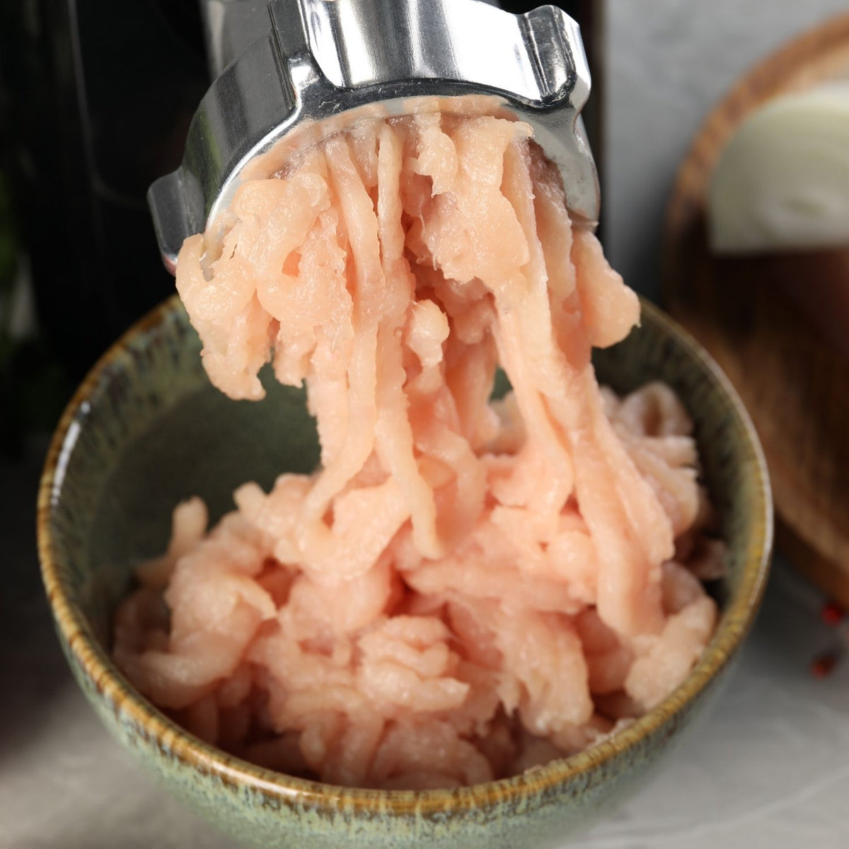 Minced chicken thigh being pressed out of a metal grinder into a bowl. - Wholesale Australian Hormone Free Chicken Thigh Mince (400g) | Buy 20 Get 6 Free